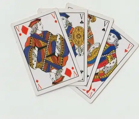 Main sujet: quatre cartes à jouer (Rami) disposées en tas, montrant des figures royales colorées. alt: Jeu de cartes Rami avec quatre cartes royales superposées. regle rami.